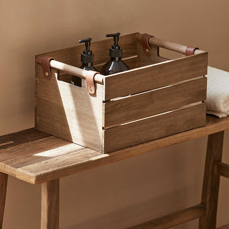 Wooden crate with leather handles on a wooden surface against a beige wall