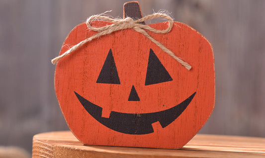 Wooden pumpkin decoration with a smiling face on a wooden surface.